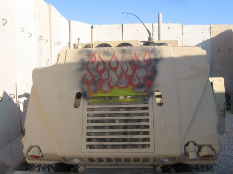 1979 Ford Bronco - A military vehicle is parked between concrete barriers, flame decals on its front.