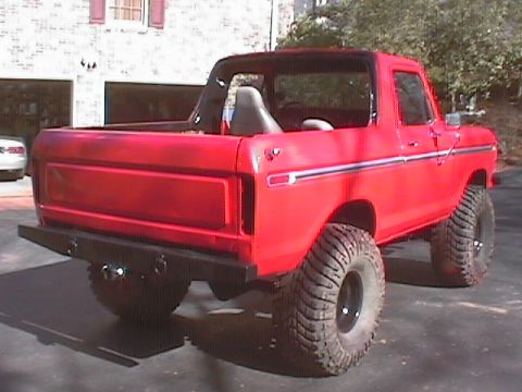 1979 Ford Bronco - This red Ford Bronco, likely a 1978 model, is shown from a rear angle with its large off-road tires and custom bumper.