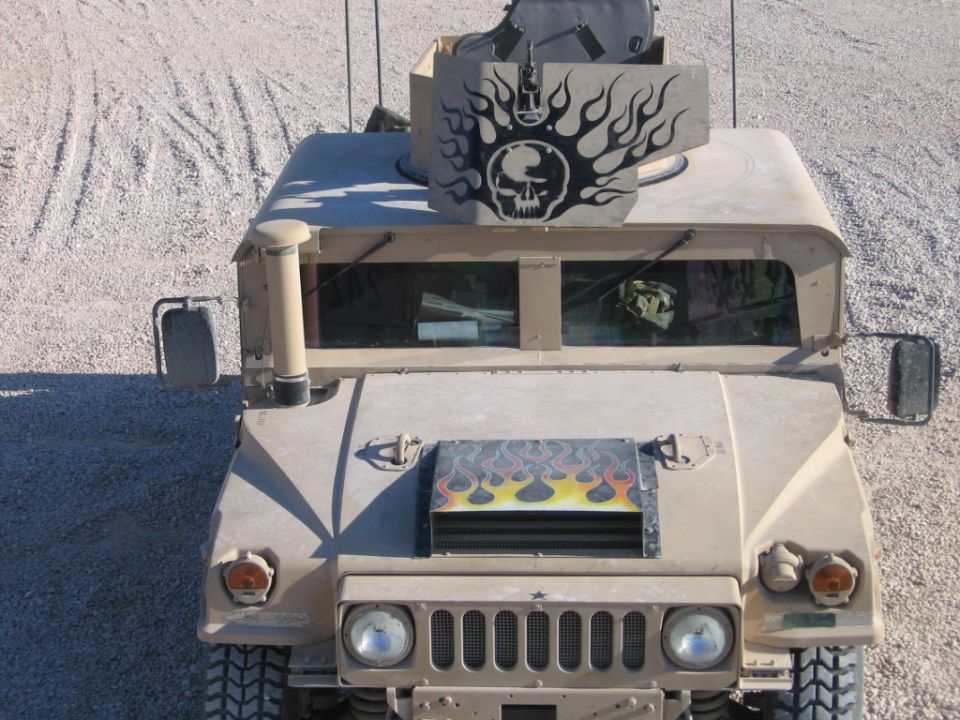 Tan military vehicle front view with skull and flames decal on roof and hood