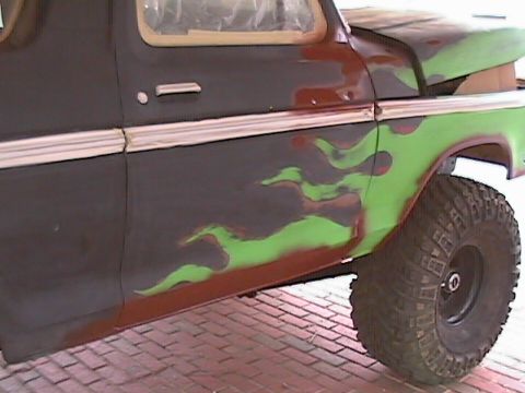 1979 Ford Bronco - Side view of a Ford truck body in primer with green and dark red flame graphics laid out across the door and front fender, masking tape sti…