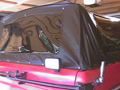 1979 Ford Bronco - A red SUV is seen from the rear with its black soft top up and a side mirror attached.