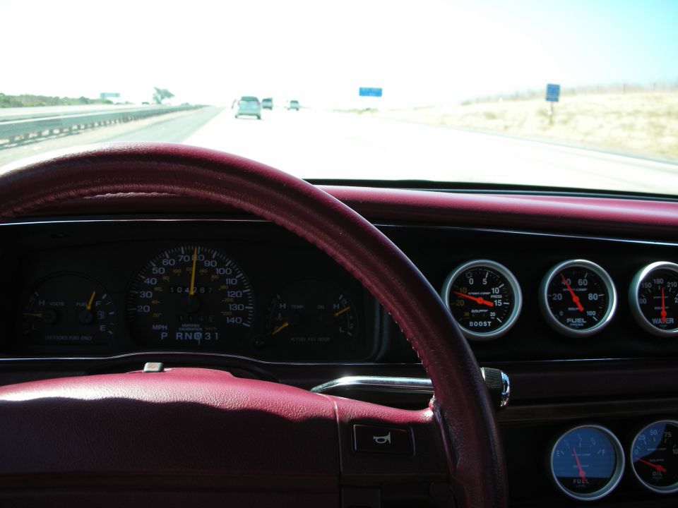 Interior dashboard with burgundy steering wheel, speedometer, and multiple gauges including boost, fuel, and water