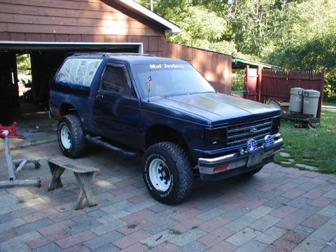 1998 Ford Taurus - This lifted SUV is parked on a brick driveway in front of a wooden garage with trees in the background.
