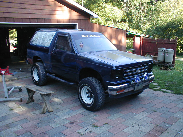 Blue SUV with lifted suspension and off-road tires parked in front of a garage