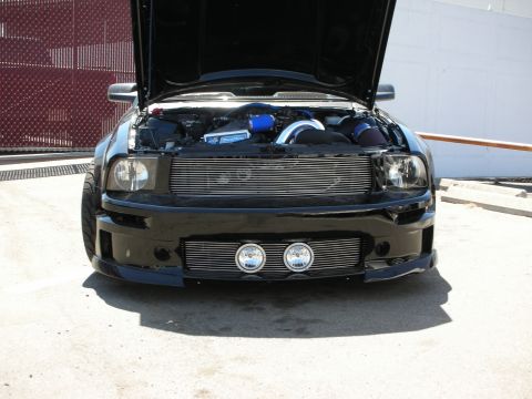 1992 Ford Crown Victoria - Head-on view of a black Mustang with the hood raised, showing a billet upper and lower grille, round driving lights in the lower valance, a…