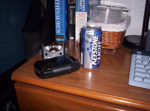 Black cell phone and Keystone Light can on a wooden desk with books and a keyboard