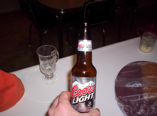 Hand holding Coors Light bottle next to an empty glass on a table