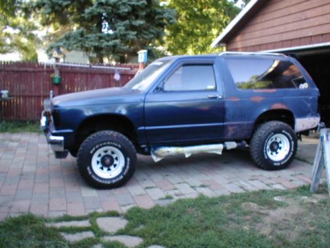 1998 Ford Taurus - Blue SUV with off-road tires parked on a brick driveway next to a garage.