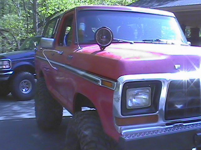 Red pickup truck with a spotlight on the hood, parked next to a blue pickup truck