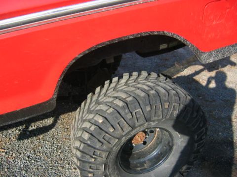 1979 Ford Bronco - Close-up of the rear wheel and fender of a red 1979 Ford Bronco, aggressive off-road tires and chrome trim.