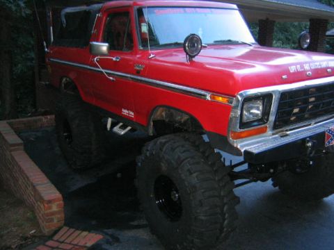 1979 Ford Bronco - Modified red Ford Bronco with large off-road tires and custom bumper.