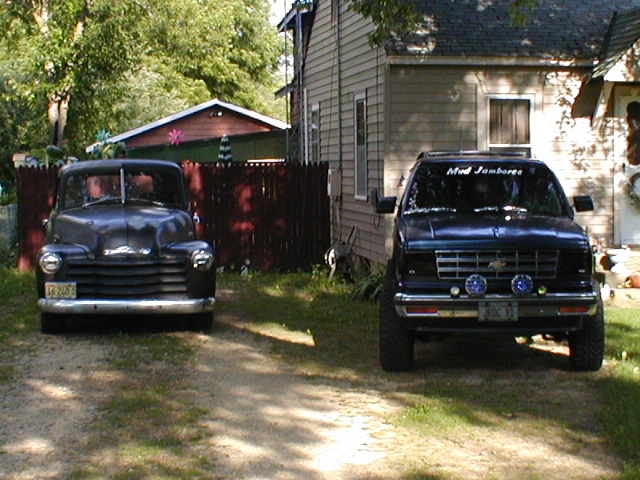 Front view of two dark trucks parked in a driveway, one older model and one newer