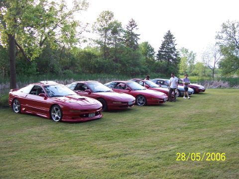1996 Ford Probe - A group of red Ford Probe cars are gathered on a lawn with trees in the background.