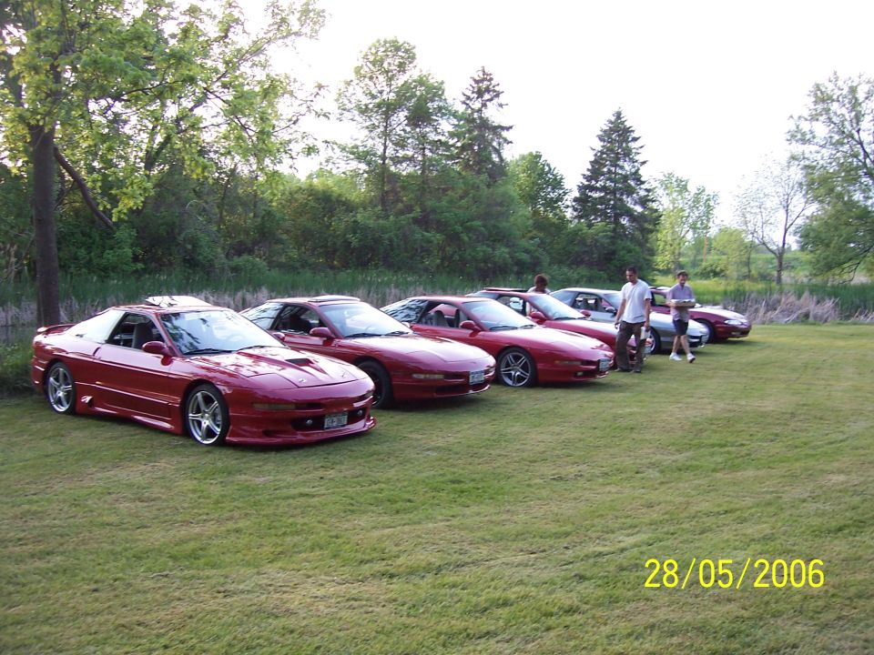 Several red Ford Probe cars parked in a line on a grassy field