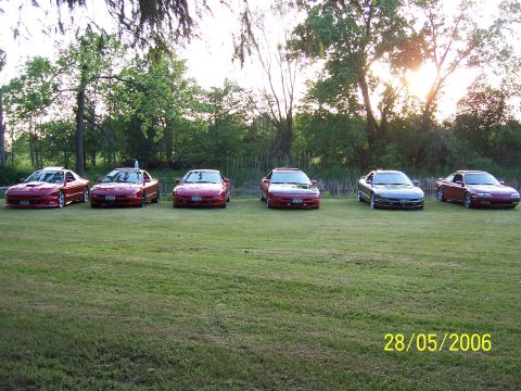 1996 Ford Probe - A group of six coupes, mostly red with one gray, are parked in a grassy area with trees in the background. The photo is dated 28/05/2006.