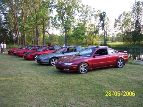 1996 Ford Probe - Several Mazda MX-6 coupes are lined up on a grassy field next to a pond.