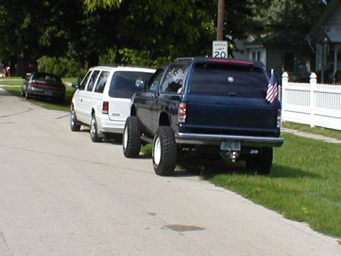 1998 Ford Taurus - A lifted pickup truck and a minivan are parked on a residential street.