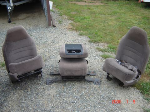 1993 Ford Bronco - Two taupe fabric captain's chairs and a center jump seat with console are laid out on gravel.
