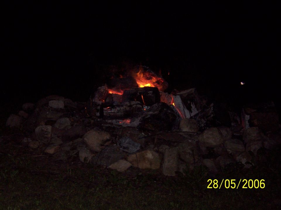 bonfire with glowing embers and flames at night, surrounded by rocks and grass