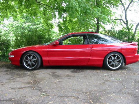 1996 Ford Probe - A red 1996 Ford Probe is parked outdoors under leafy trees, showing its side profile.