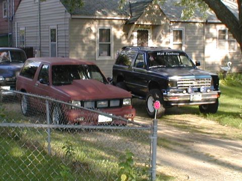 1998 Ford Taurus - A red pickup truck sits parked in front of a residential building next to another vehicle.