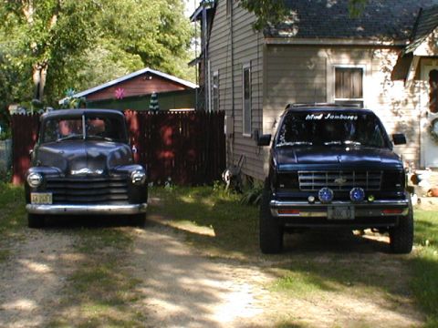 1998 Ford Taurus - Two trucks are parked in a residential driveway on a sunny day.