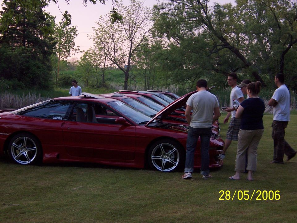 Red coupes lined up with hoods open, people gathered around