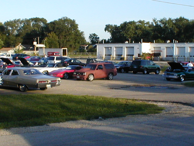 Parking lot filled with various cars and SUVs, some with hoods open