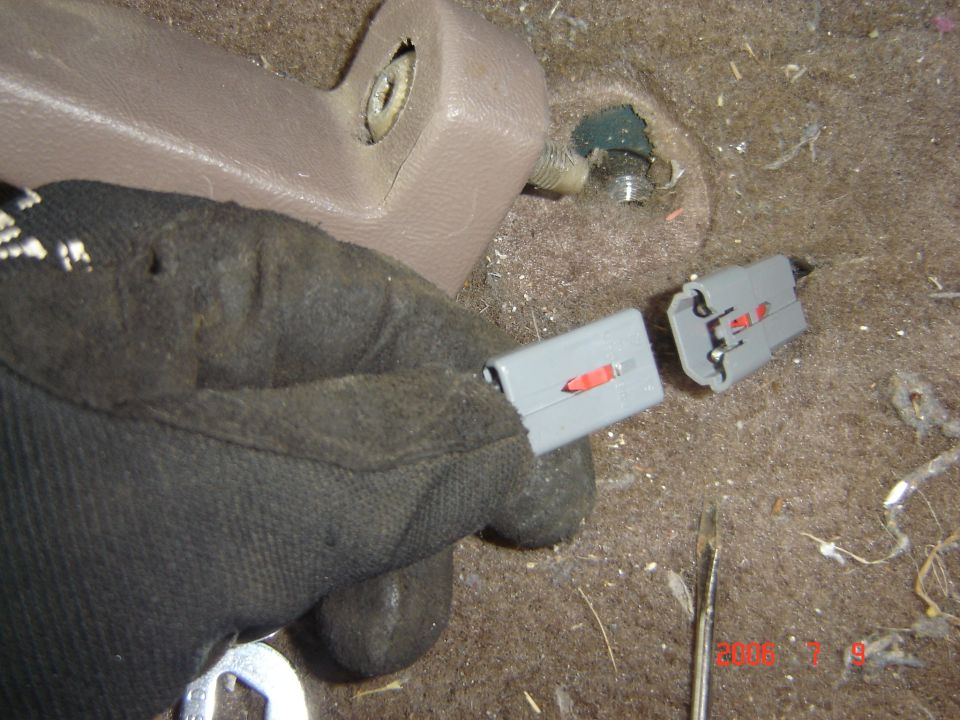 Gloved hand holding a gray electrical connector pigtail near tan trim panel