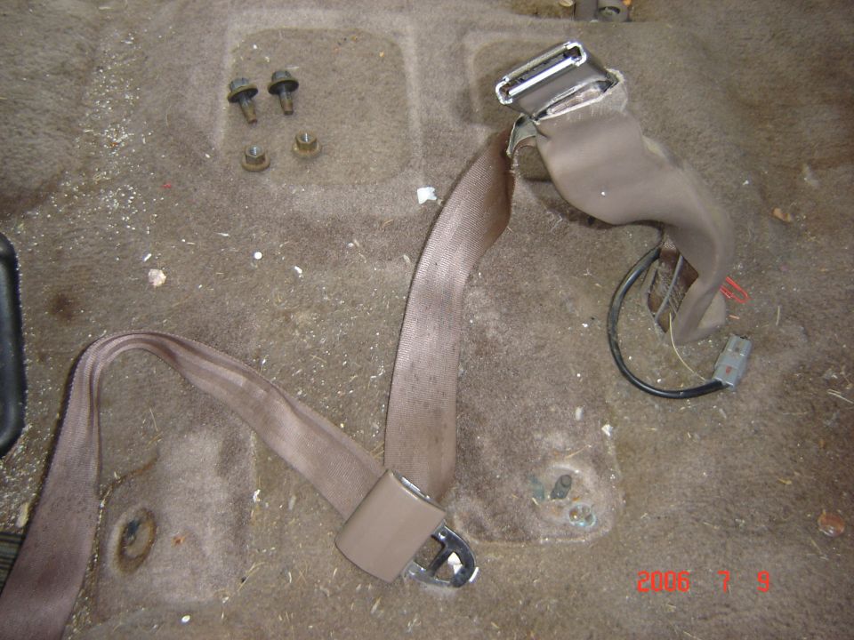 Tan seatbelt assembly with buckle and retractor lying on gray carpet with mounting hardware