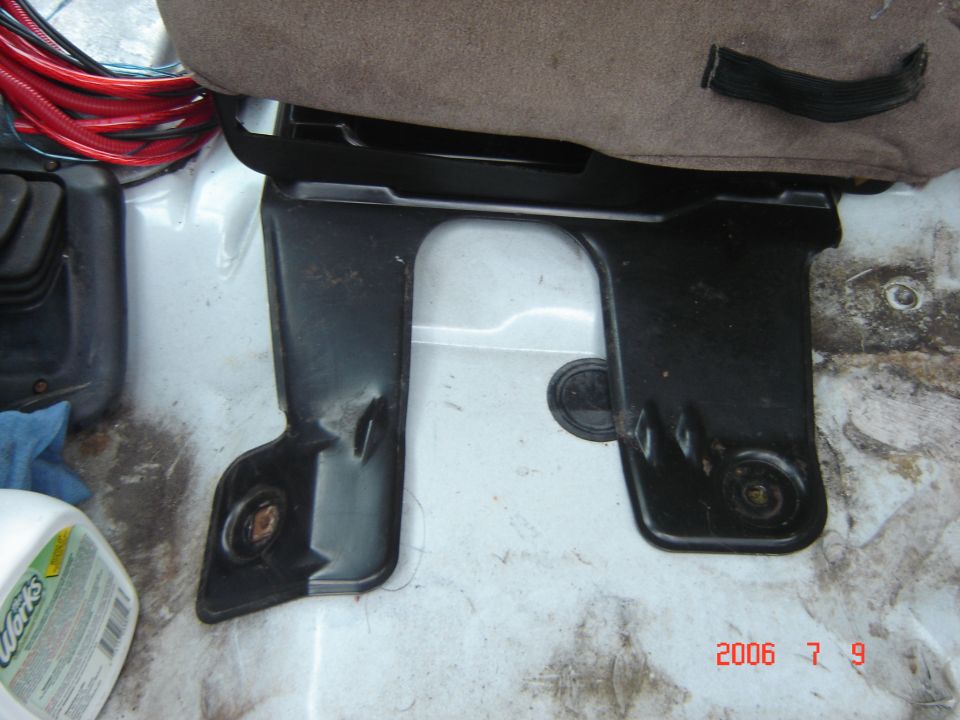 Black jumpseat mounting bracket bolted to white vehicle floor with brown seat cushion above.