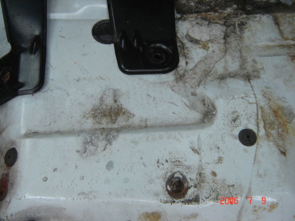 Dirty white vehicle floor pan with corroded mounting studs and black components