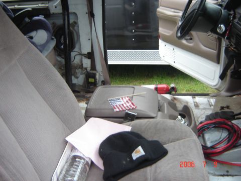1993 Ford Bronco - The interior of a vehicle shows tan seats, a center console, and various items scattered around.