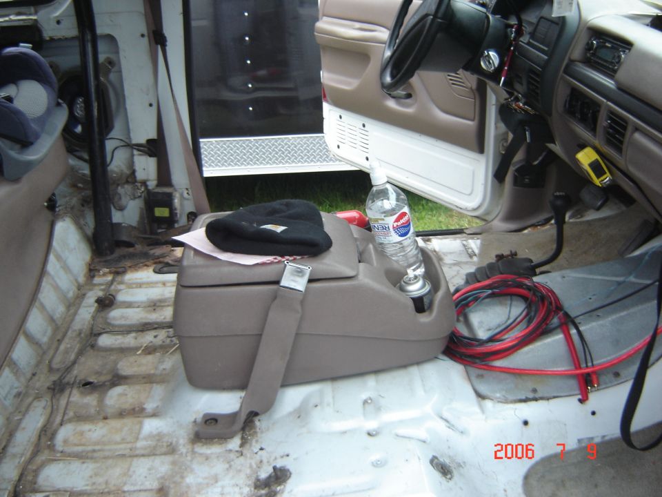 Truck interior with passenger seat removed, tan console, jumper cables, open door