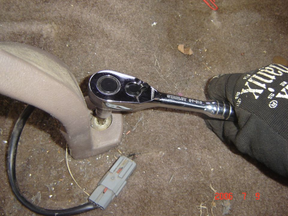 Gloved hand using Stanley ratchet on bolt of tan seatbelt receptacle mount