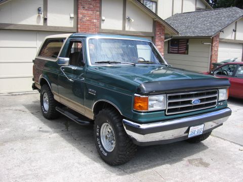 1990 Ford Bronco - Green Ford Bronco with tan trim and roof parked in front of a garage.