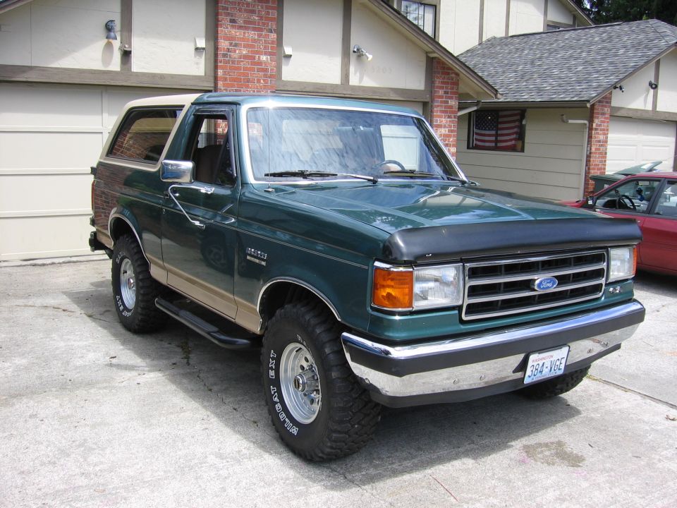 Green Ford Bronco with tan lower body trim and a tan removable roof, parked in a driveway