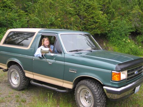 1990 Ford Bronco - A woman smiles from the driver's seat of a green 1990 Ford Bronco parked outdoors.