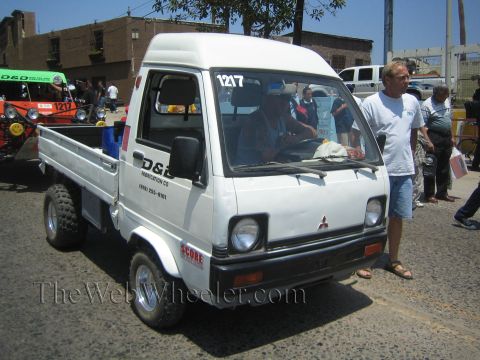 1990 Ford Bronco - small white Mitsubishi mini cab-over pickup number 1217 with D&S graphics parked among spectators on pavement.