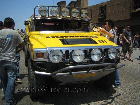 1990 Ford Bronco - Front view of a yellow Hummer H2 number 861 with a roof-mounted light bar and four Lightforce driving lamps amid a crowd.