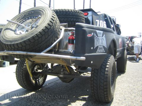 1990 Ford Bronco - Rear view of a desert race truck number 706 carrying two spare tires, a fire extinguisher and Pro Tek graphics in a pit lot.