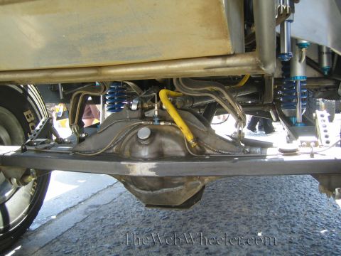 1990 Ford Bronco - Underside view of an off-road vehicle's rear end with a center differential, blue coilover shocks and yellow brake/bypass lines.