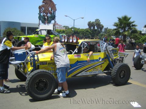 1990 Ford Bronco - yellow and blue tube-frame off-road race buggy number 1170 with BFGoodrich graphics among crew and spectators on a street.