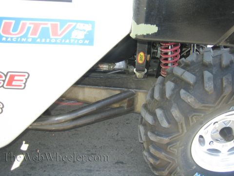 1990 Ford Bronco - Close-up of a side-by-side UTV's rear suspension showing a red coilover shock, A-arm and knobby off-road tire.