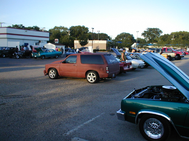 red SUV parked at car show, other cars around, one with hood open