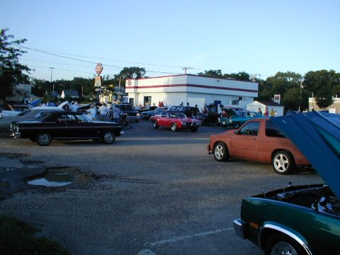 1998 Ford Taurus - Cars are gathered in a parking lot outside a building on a clear day.