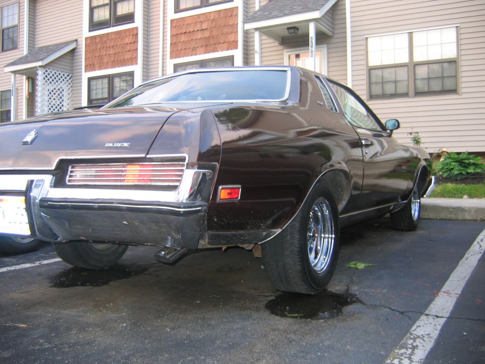 Dark brown Buick coupe, rear 3/4 view, chrome wheels, parked on wet lot