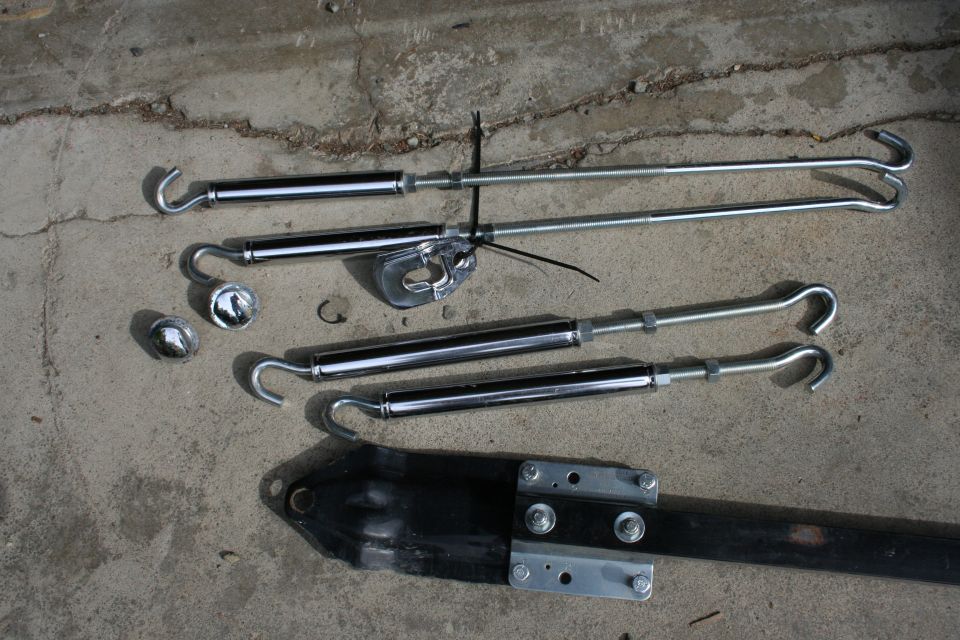 Four chrome tie-down straps with hooks and a black metal bracket on concrete