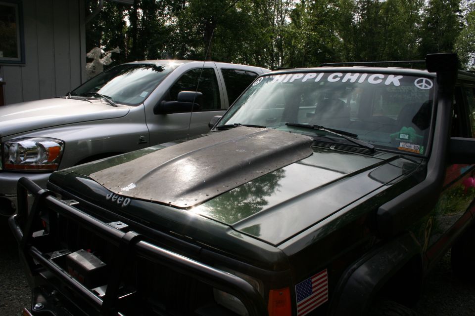 Dark green 1995 Jeep Cherokee with a scoop hood and snorkel, parked next to a silver pickup truck