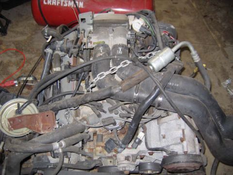1986 Ford C-350 (Centurion Conversions) - A disassembled engine sits on a floor, surrounded by various hoses and wiring harnesses.